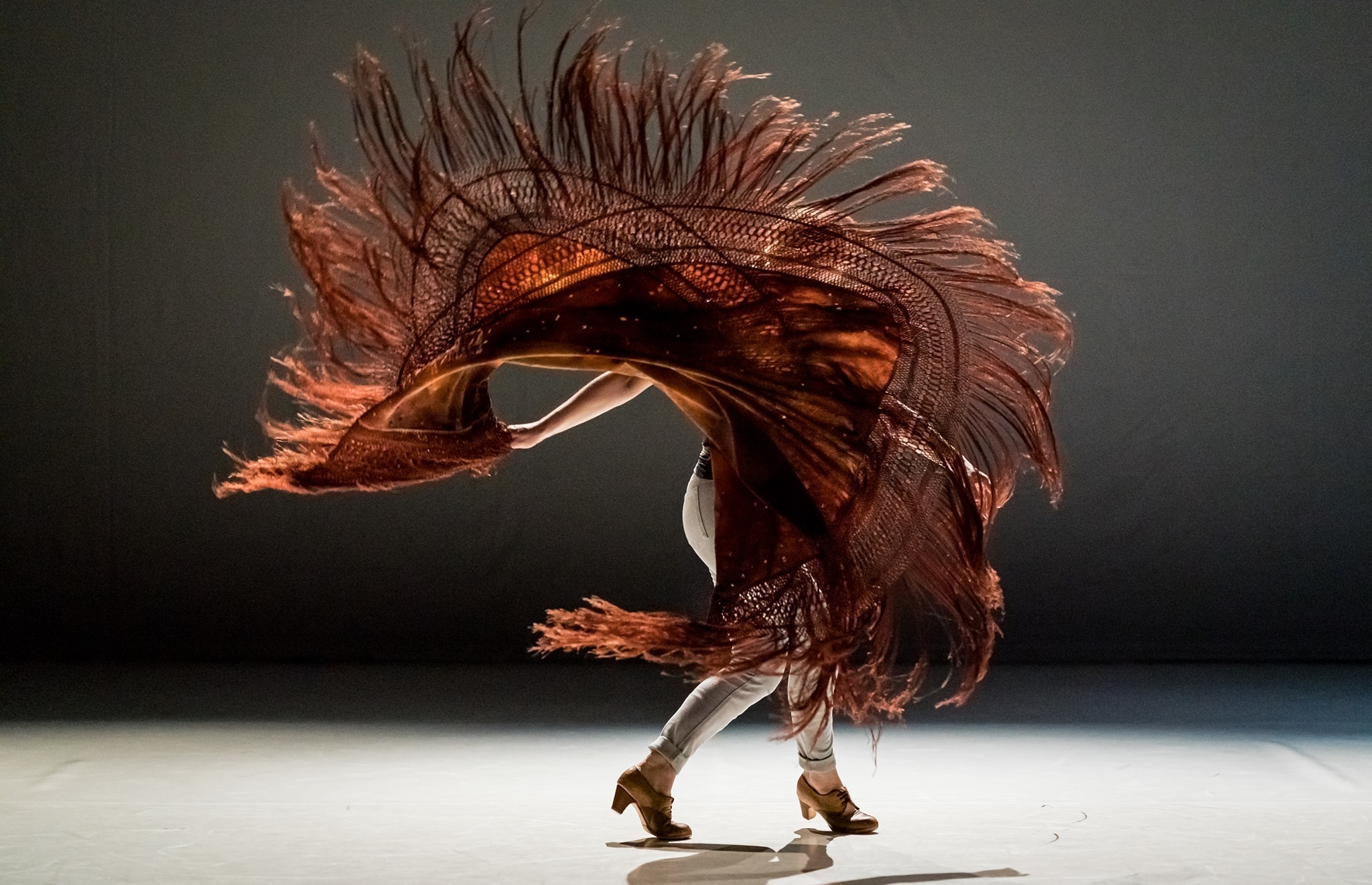 A flamenco dancer with a huge red shawl flung up in front of them so you can only see some of their legs and their feet.